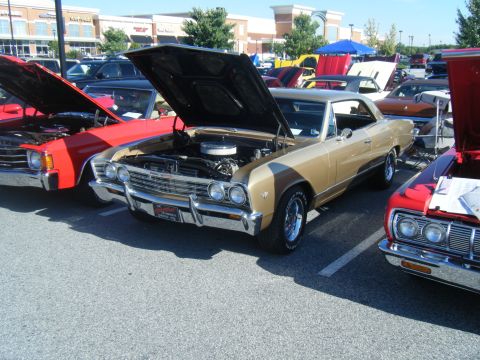 1991 Nissan Micra - A gold and tan 1967 Chevrolet Chevelle coupe is displayed with its hood open at an outdoor car event.