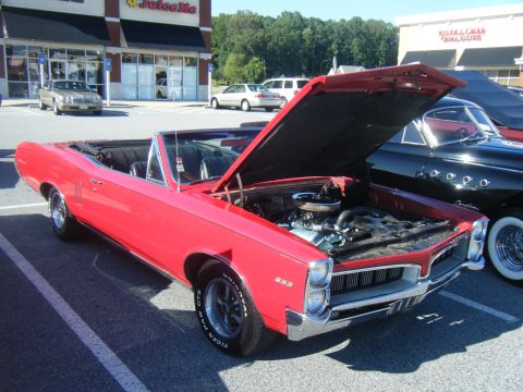 1991 Nissan Micra - Red 1966 Pontiac Tempest convertible parked in a lot, hood open showing the engine.