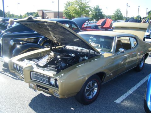 1991 Nissan Micra - Gold 1969 Pontiac GTO at a car show, hood and trunk open, with other vehicles nearby.