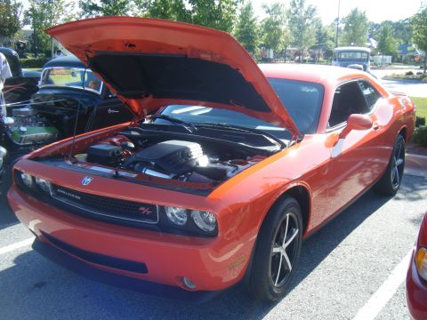 1991 Nissan Micra - An orange Dodge Challenger is parked with its hood open, revealing the engine bay. Another vehicle is visible to the left.