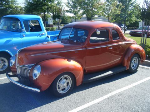 1991 Nissan Micra - A classic orange coupe is parked next to a blue pickup truck on a sunny day.
