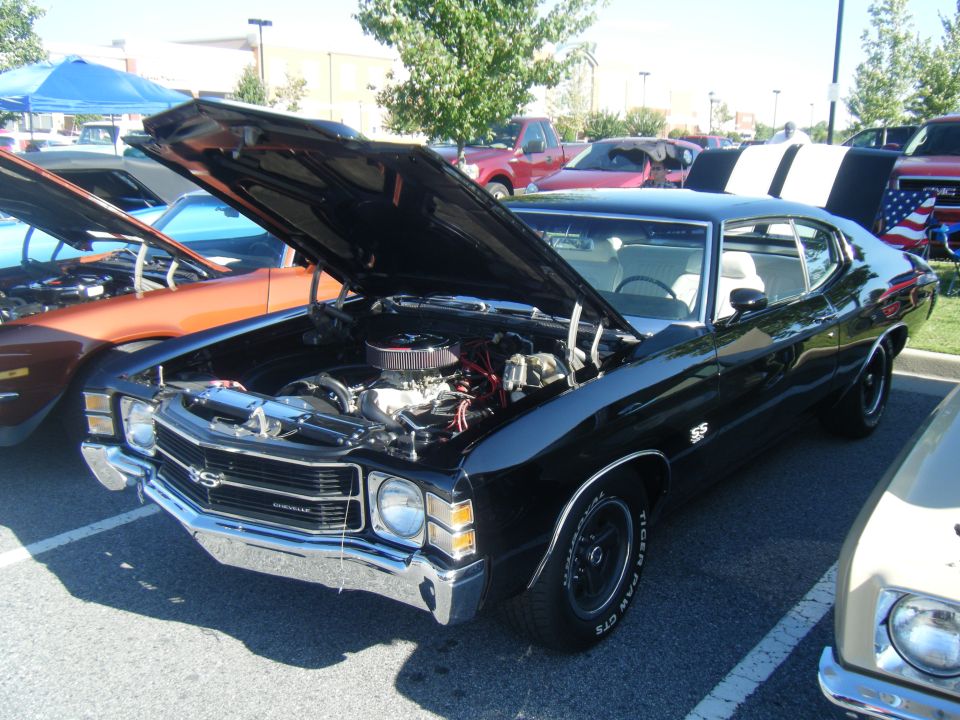Black 1970s muscle car, SS badging, hood open showing engine, parked outdoors