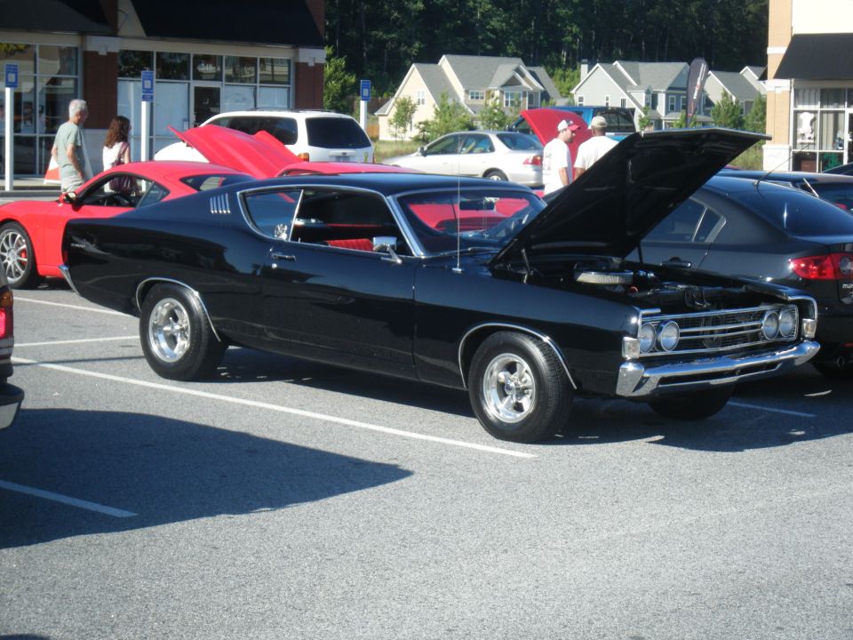 Black classic coupe with hood open, red interior, chrome wheels. Another red car is parked to the left