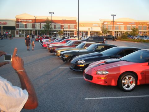 1991 Nissan Micra - A line of cars are parked in a lot in front of a strip mall.