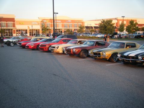 1991 Nissan Micra - A row of vintage American muscle cars, likely Camaros, are parked in a lot with buildings in the background.