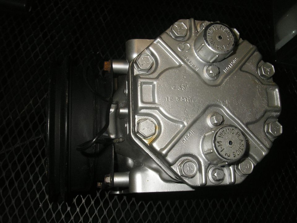 Close-up of a silver air conditioning compressor with visible bolts and some text on caps