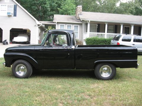 1966 Ford F-100 - A black 1965 Ford F-100 pickup truck is parked on a lawn in front of a residential home.