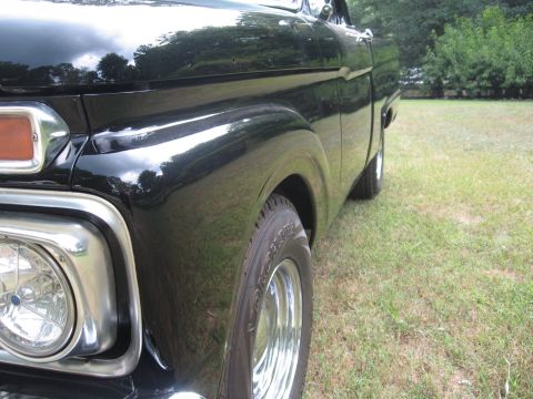 1966 Ford F-100 - Close-up of the front quarter panel and headlight on a black 1966 Ford F-100 pickup truck.