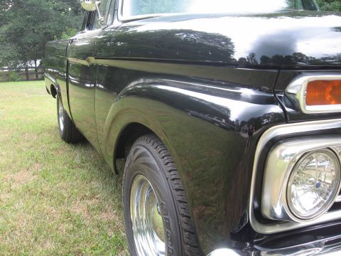 1966 Ford F-100 - A black pickup truck is viewed from the front quarter angle, highlighting its classic design elements.