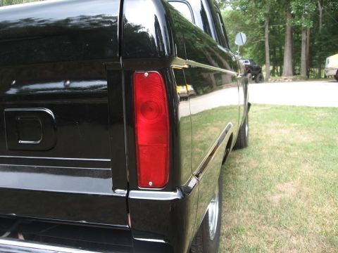 1966 Ford F-100 - The rear quarter panel and taillight of a black 1966 Ford F-100 pickup truck are visible, with another vehicle in the background.