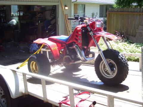 1991 Ford Bronco - A red three-wheeled ATV is secured with yellow straps to a trailer in front of a garage.