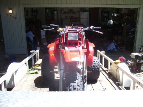 1991 Ford Bronco - A red three-wheeled ATV is parked on a wooden trailer in front of a garage.