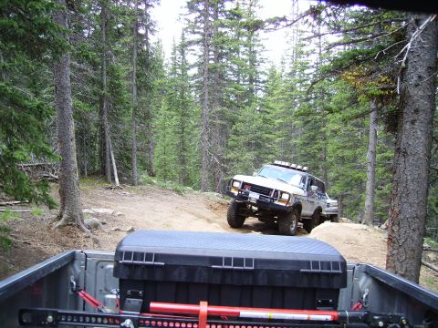 1978 Ford Bronco - A 1978 Ford Bronco navigates a wooded trail, viewed from the bed of another vehicle.