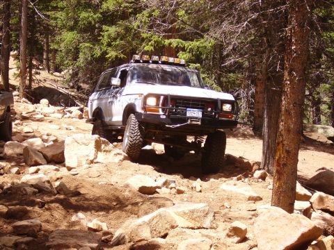 1978 Ford Bronco - White 1978 Ford Bronco tackling a challenging off-road course in a wooded area.