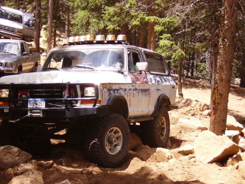 1978 Ford Bronco - This lifted Ford Bronco navigates a challenging, rocky off-road path in a wooded area.
