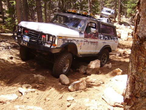 1978 Ford Bronco - A 1978 Ford Bronco navigates a rocky, wooded trail with other vehicles behind it.