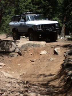 1978 Ford Bronco - A 1978 Ford Bronco navigates a challenging off-road path through a forest.