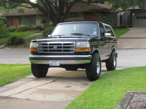 1994 Ford Bronco - This black Ford Bronco is parked on a concrete driveway in front of a residential house.