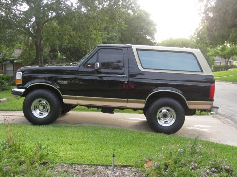 1994 Ford Bronco - Side view of a black Ford Bronco with tan accents, parked on a paved surface next to a lawn.