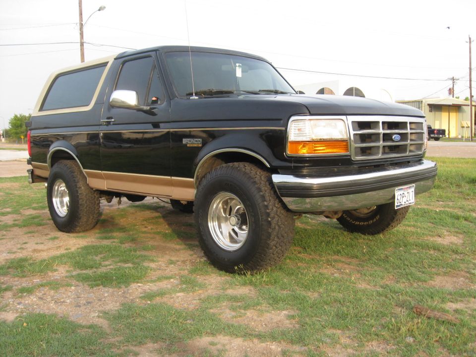 Black Ford Bronco with tan trim, lifted suspension, and chrome wheels parked on grass