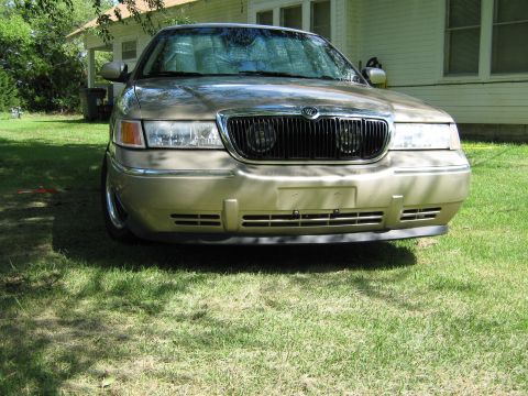 2000 Mercury Grand Marquis - A gold Mercury Grand Marquis is parked in front of a house on a sunny day.