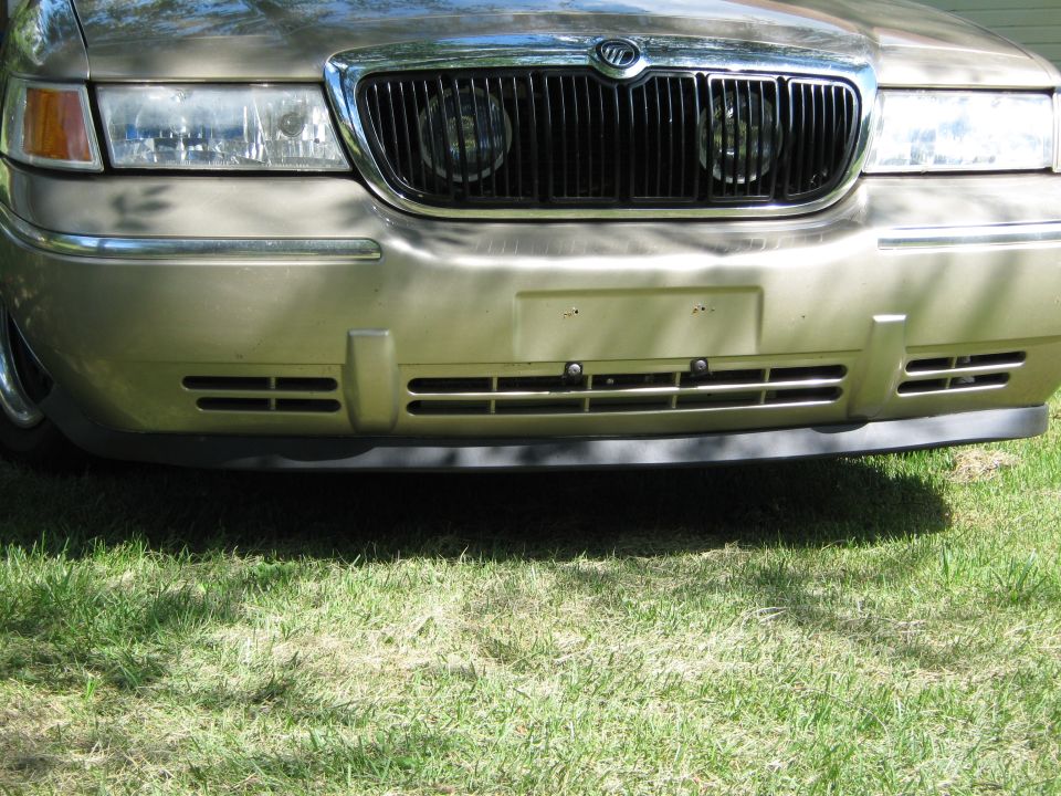 Front bumper close-up of gold Mercury with grille-mounted driving lights and black air dam