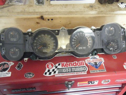 1991 Nissan Micra - Instrument cluster with speedometer, tachometer, fuel, and voltage gauges. Toolbox below has various stickers.