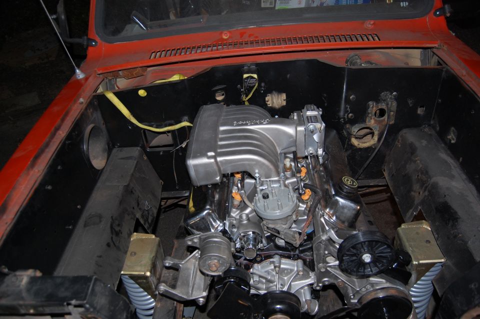 Engine bay showing a V8 engine with a silver intake manifold and orange fuel injectors. The vehicle is red