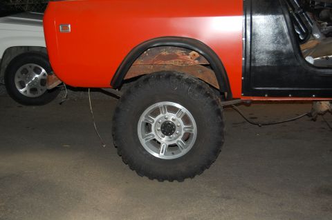 1994 Ford Bronco - An orange and black SUV is shown from the side, with a large tire and fender detail. A white vehicle is also visible.