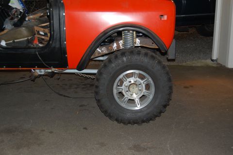 1994 Ford Bronco - Side view of an orange off-road vehicle with a large tire and visible suspension components.