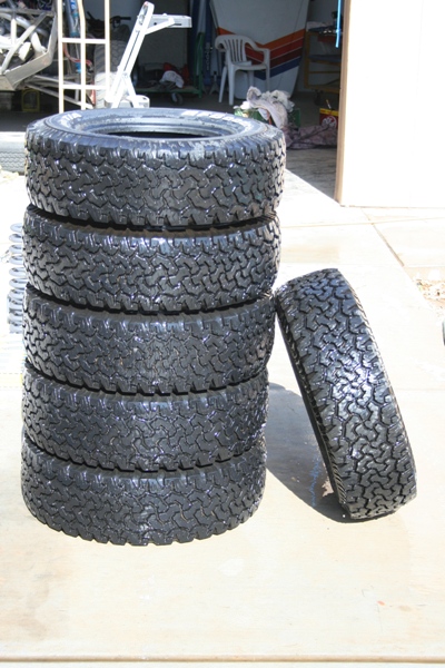 1989 Ford Bronco - Five off-road tires are stacked vertically, with one tire leaning on the side.