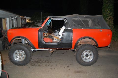 1994 Ford Bronco - This orange off-road vehicle features black doors and a black soft top, seen from the side.