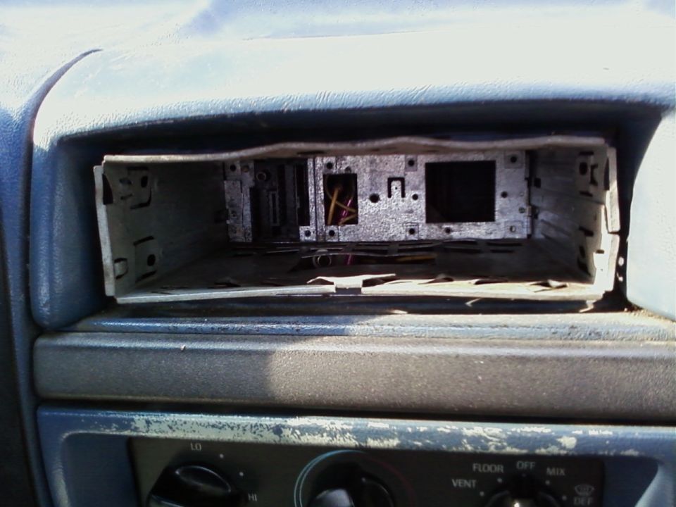 Removed car stereo mount in a blue dashboard with exposed wires and metal brackets