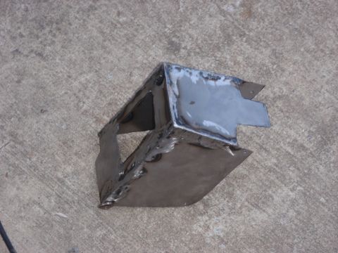 1996 Ford Bronco - A shop-fabricated bare-steel bracket sitting on a concrete floor, built from cut plate with notched tabs and a boxed pocket, joined by stac…