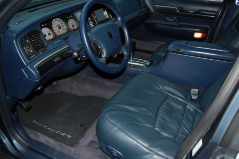 1985 Mercury Grand Marquis - The interior features blue leather seats, a Marauder branded floor mat, and a dashboard with prominent gauges.