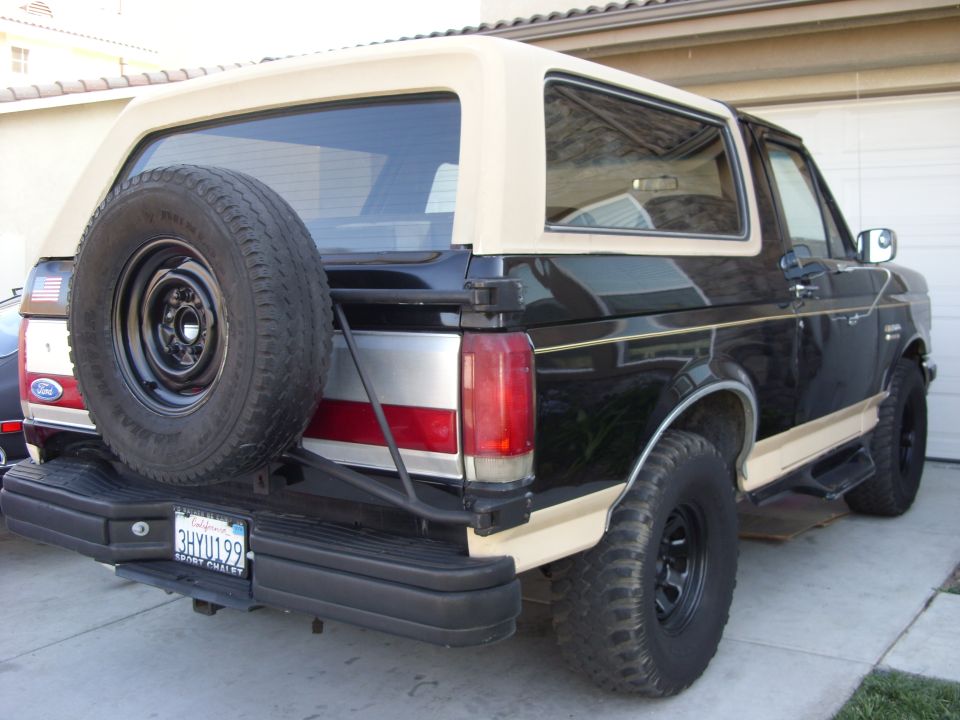 Rear view of a black 1989 Ford Bronco with a tan top and spare tire