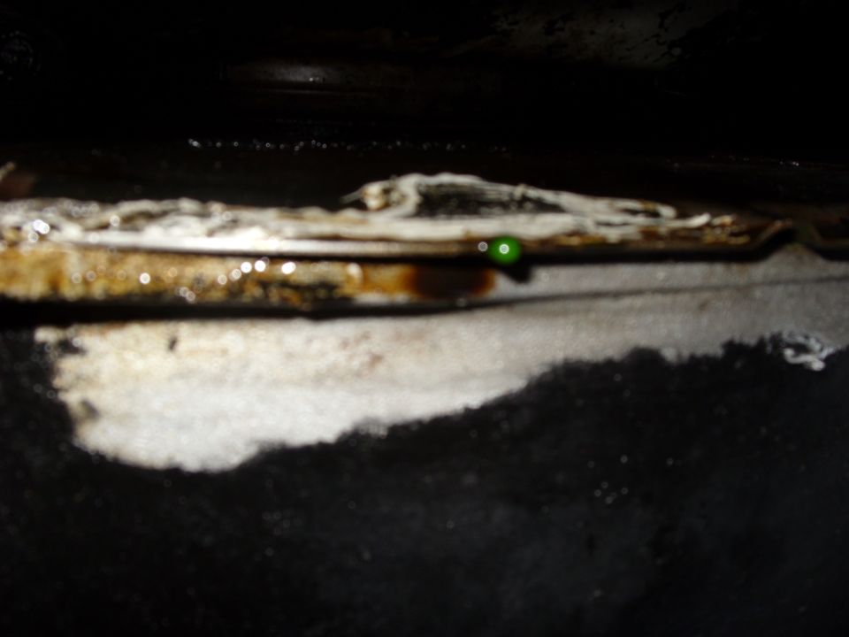 Close-up of engine oil leak with green fluid drip