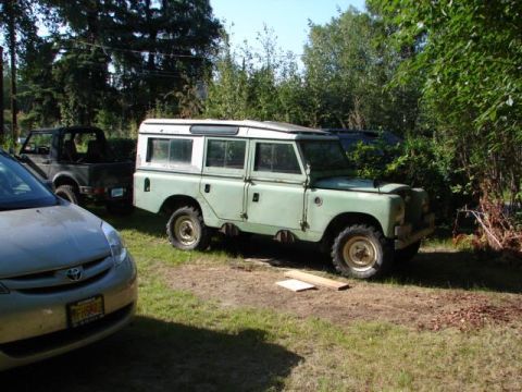 1967 Land Rover Land Rover - A light green Land Rover Series III with a white roof is parked outdoors next to other vehicles.