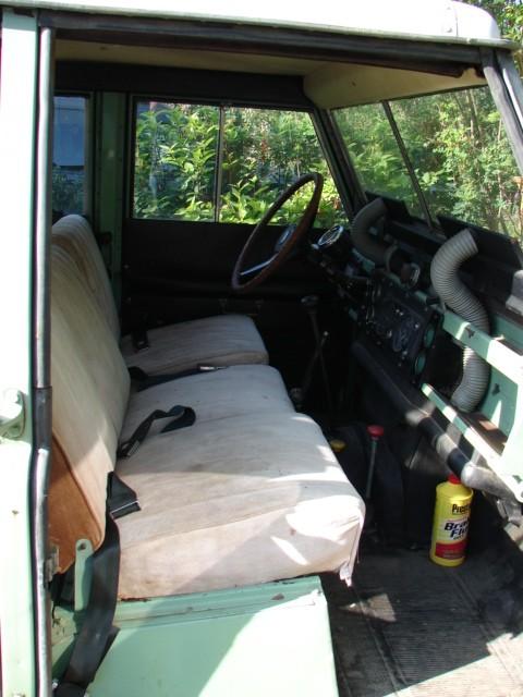 1967 Land Rover Land Rover - The interior of a 1967 Land Rover features a bench seat, dashboard, and steering wheel, with a bottle of Prestone visible on the floor.