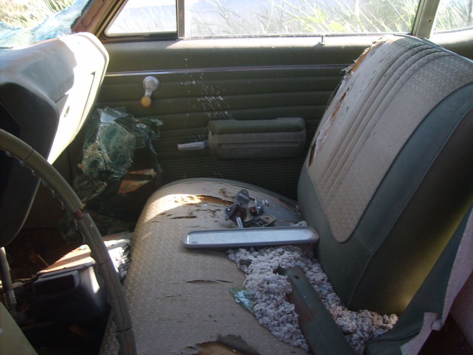 Interior of a car with torn seats, broken windshield, and exposed insulation