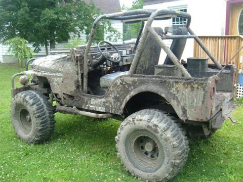 1976 Jeep CJ5 - This heavily mud-caked 1976 Jeep CJ5 is viewed from the front-right, showing its off-road modifications and weathered condition.