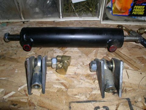 1979 Ford Bronco - Hydraulic cylinder and associated mounting hardware are laid out on a wooden surface. The registry claims this is for a 1979 Ford Bronco.