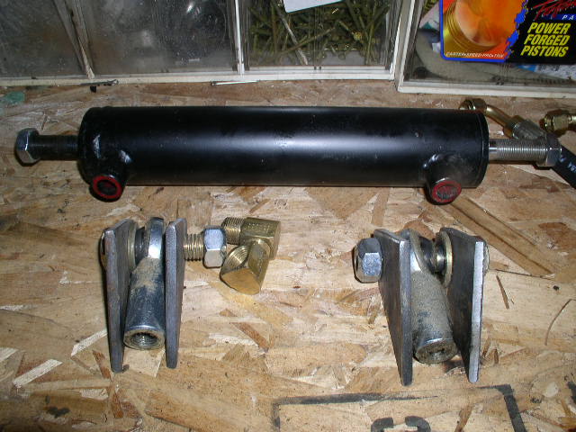 Black hydraulic ram cylinder, steel mounting brackets and brass fittings on a workbench