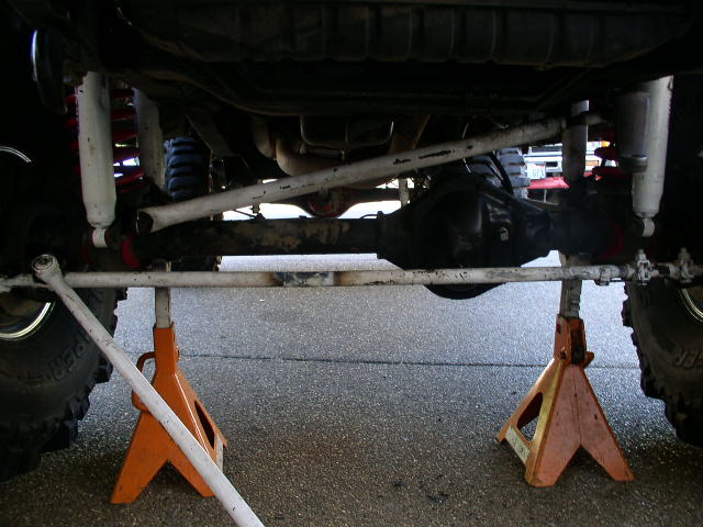 Underbody of lifted 4x4 on orange jack stands showing solid axle, radius arms and shocks