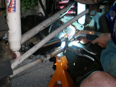 1979 Ford Bronco - A person welds suspension parts on a vehicle, with sparks flying and a shock absorber in view.