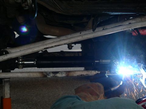 1979 Ford Bronco - A mechanic welds a steering stabilizer cylinder, likely for power steering assist, onto a vehicle's frame.