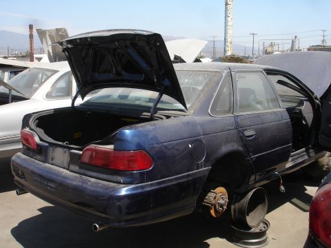 1993 Ford Taurus - Junkyard scene with a blue sedan missing wheels and parts, next to another vehicle.