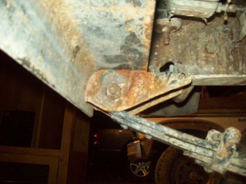1971 Ford F-100 - Close-up of a heavily rusted truck frame and suspension component, with another vehicle in the background.