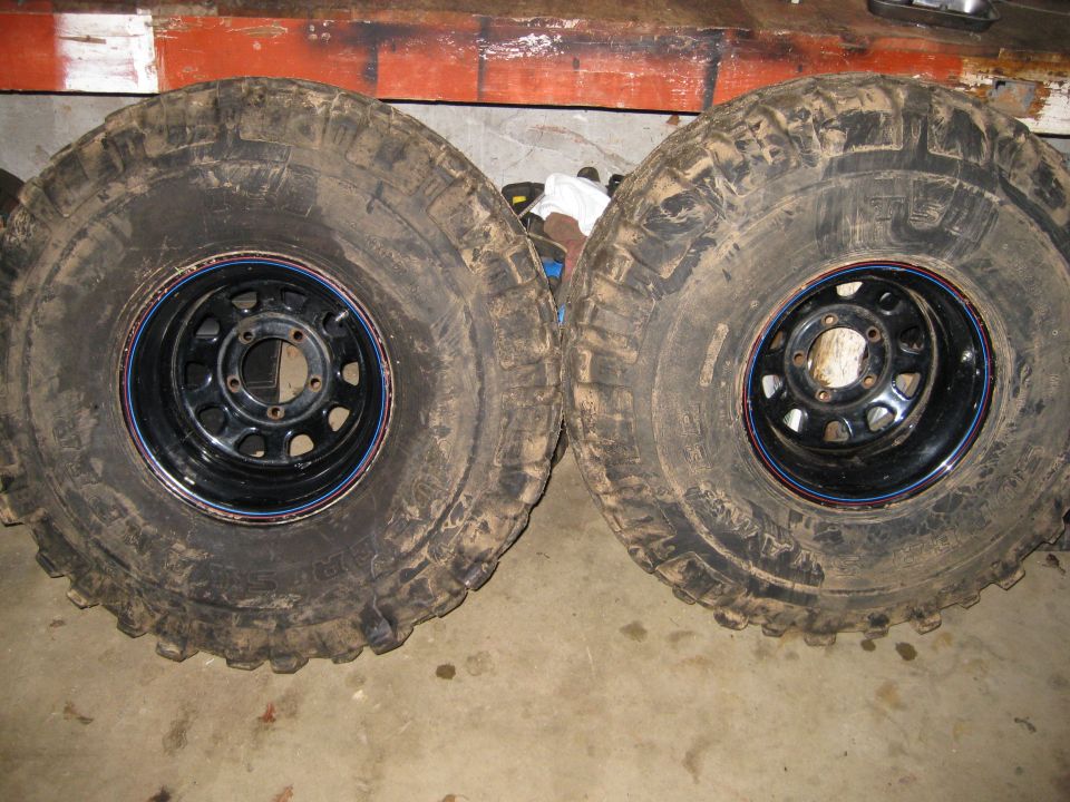 Two large off-road tires mounted on black steel wheels, resting on a concrete floor