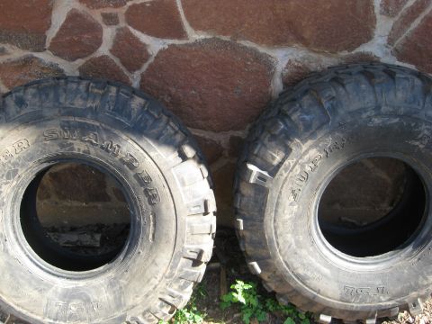 1986 Ford Bronco - Two Super Swamper tires are shown leaning against a stone wall, with some greenery at their base.
